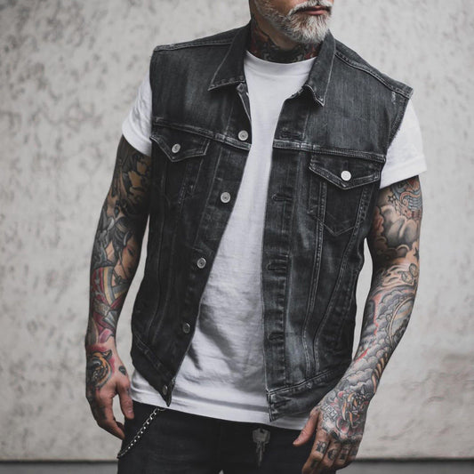 Giacca di jeans nera senza maniche su uomo tatuato, indossa maglietta bianca. Moda streetwear, stile casual, tendenze abbigliamento maschile.