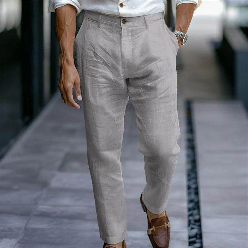Uomo in camicia bianca e pantaloni grigi eleganti, cammina su marciapiede moderno. Scarpe marroni, orologio al polso. Moda maschile urbana.