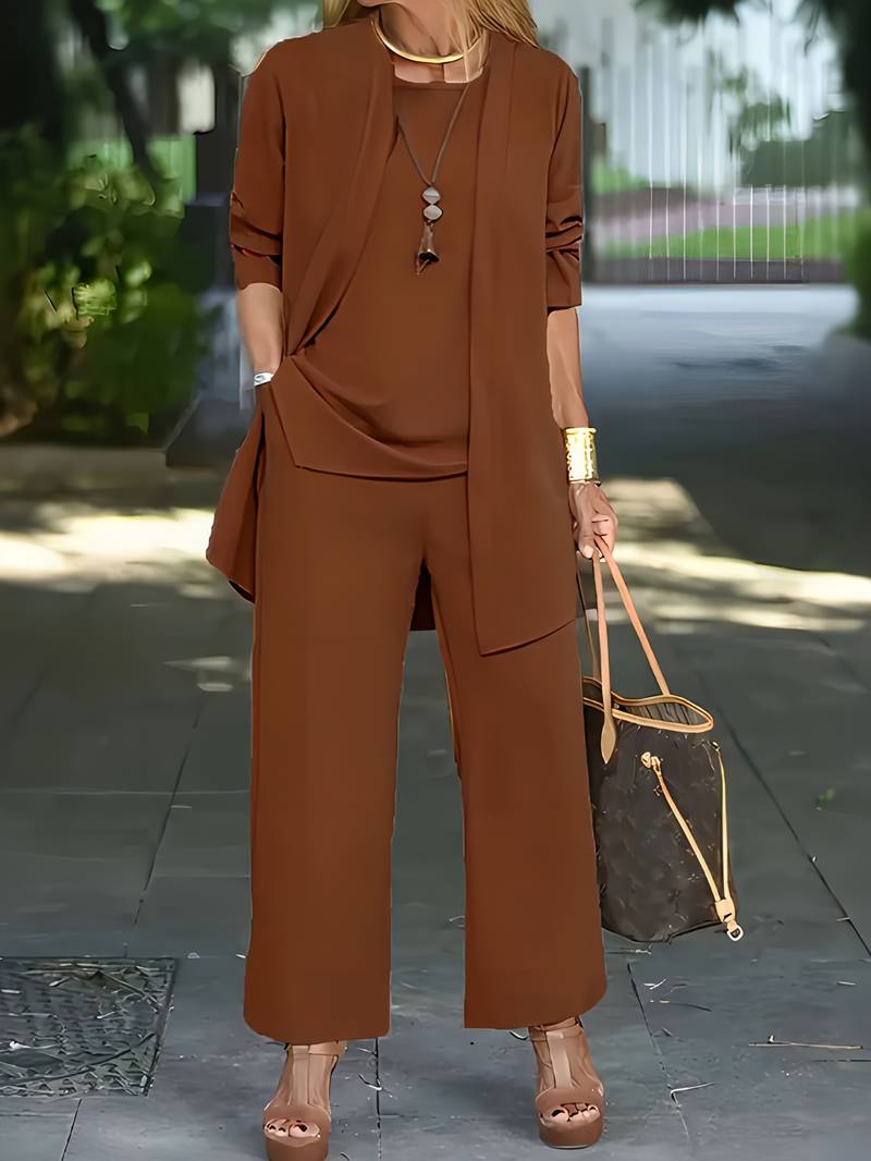 Donna in completo marrone elegante, con pantaloni larghi e giacca lunga, indossa sandali con tacco e borsa di lusso. Look moda autunnale chic.