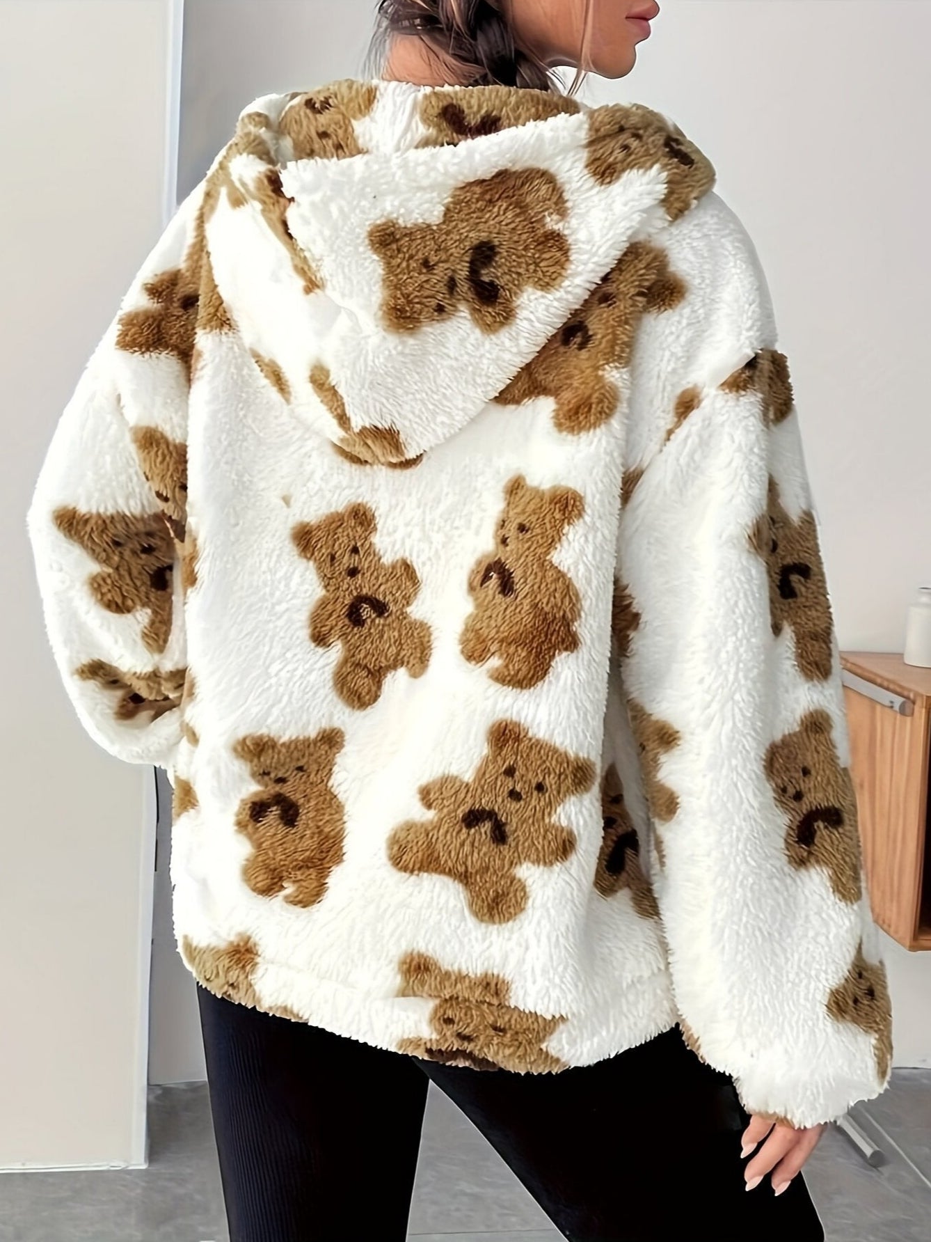 Donna con giacca in pile bianca con stampa orsetti marroni, cappuccio, pantaloni neri. Moda autunno inverno, abbigliamento casual caldo.