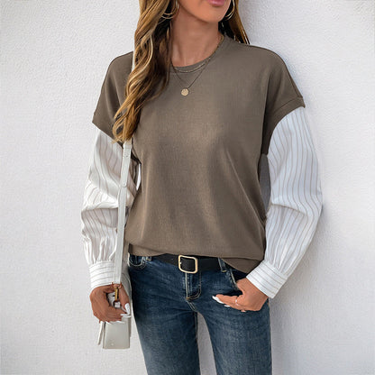 Donna con maglia a maniche lunghe marrone e bianche, jeans blu, borsa bianca, collana dorata. Moda casual autunnale, stile urbano chic.