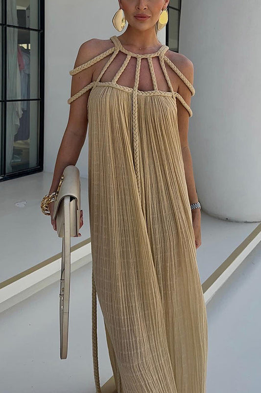 Donna con abito lungo beige plissettato, dettagli a corda, borsa a mano chiara, orecchini grandi dorati. Look estivo elegante e sofisticato.