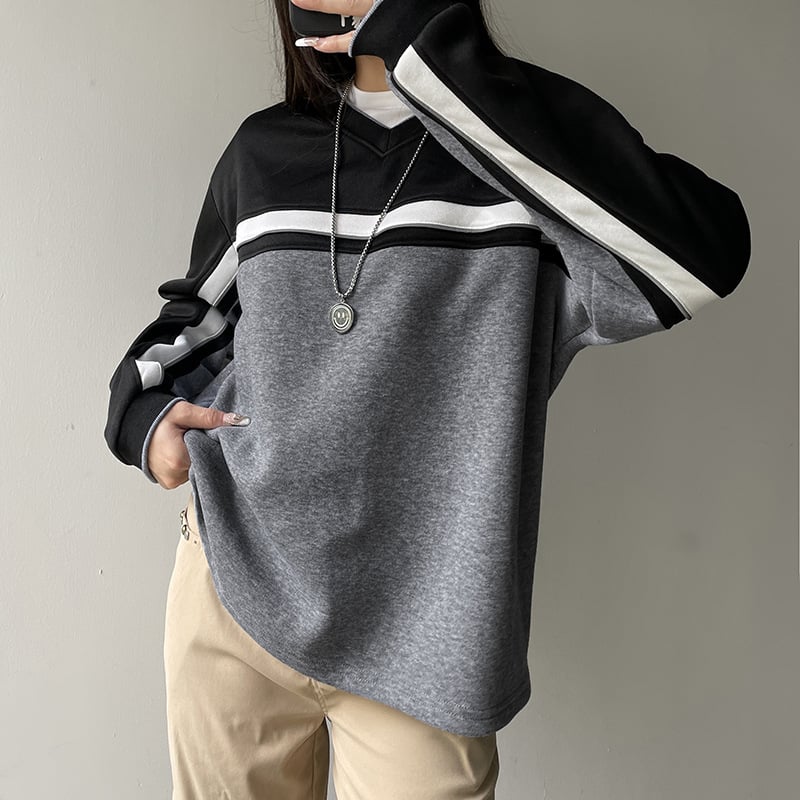Maglia oversize grigia e nera con strisce bianche, indossata da una persona. Stile casual, moda autunnale, abbinata a pantaloni beige.