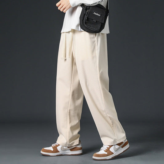 Pantaloni larghi beige uomo, abbinati a sneakers bianche e marroni, borsa a tracolla nera. Moda casual, streetwear maschile.