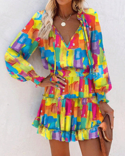 Abito estivo multicolore con fantasia astratta, maniche lunghe e scollo a V. Perfetto per look casual e vivaci. Donna con accessori dorati.