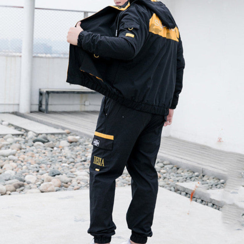 Giacca sportiva nera con dettagli gialli, indossata da uomo all'aperto. Abbigliamento casual, moda streetwear, stile urbano.