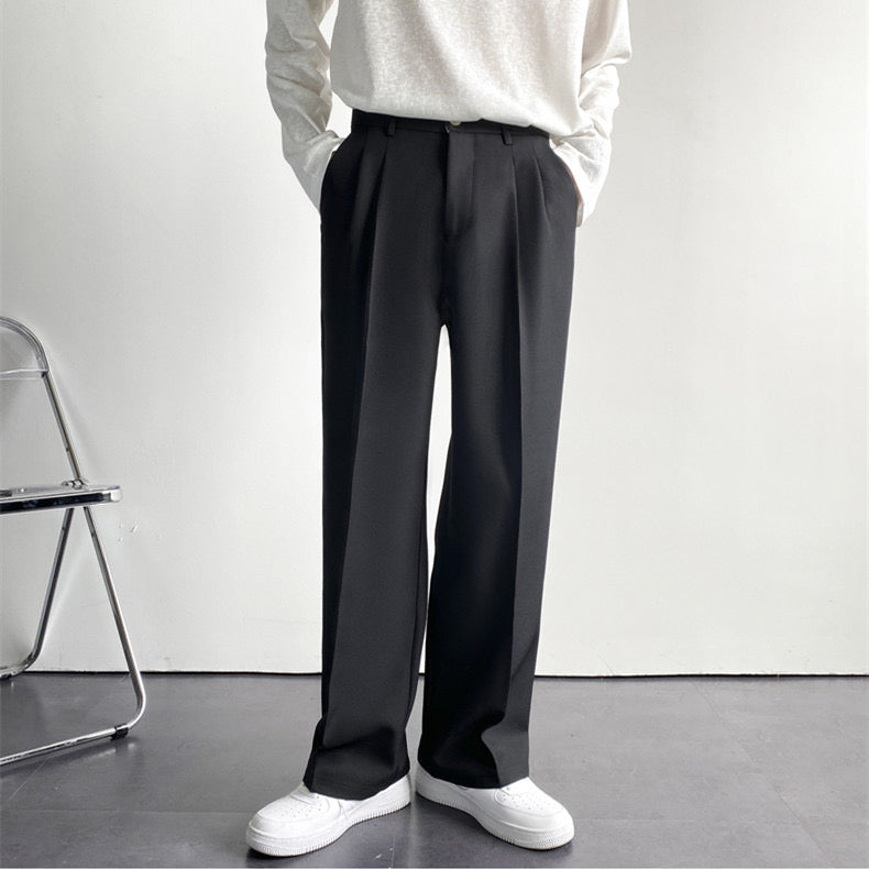 Pantaloni neri eleganti da uomo, taglio dritto, abbinati a maglia bianca e scarpe bianche, su sfondo minimalista. Moda maschile contemporanea.