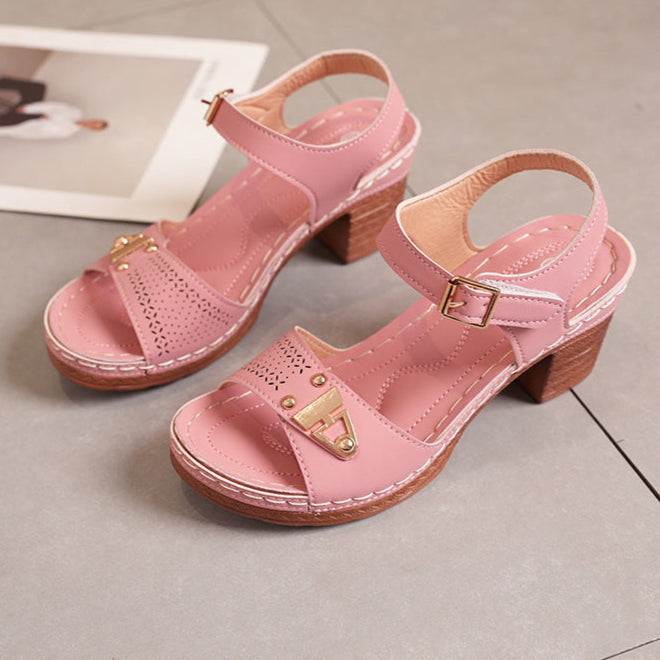 Sandali rosa con tacco largo in legno, cinturino regolabile e dettagli dorati, su pavimento grigio. Scarpe estive eleganti e comode.