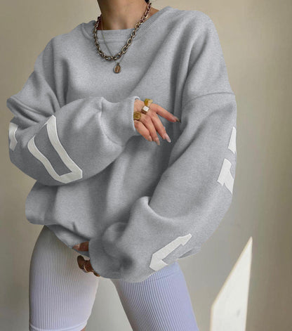 Donna con felpa grigia oversize e pantaloni a coste bianchi, indossa collana e anelli dorati. Moda casual, abbigliamento streetwear trendy.