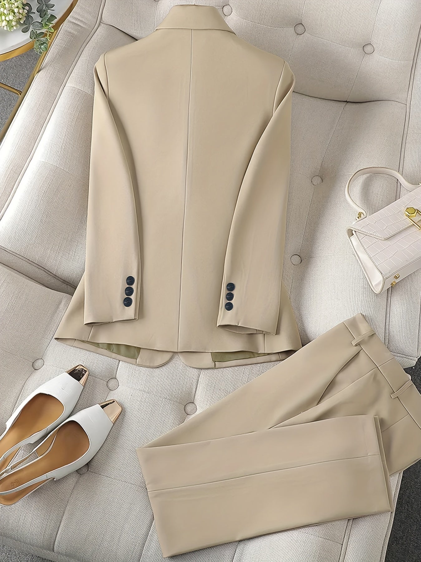 Completo elegante beige su divano, giacca e pantaloni abbinati, scarpe bianche con tacco e borsa bianca. Moda uomo, abbigliamento formale.