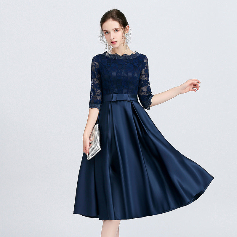 Donna in abito da sera blu scuro in pizzo e raso, con maniche a tre quarti, tiene una pochette argentata. Elegante moda femminile.