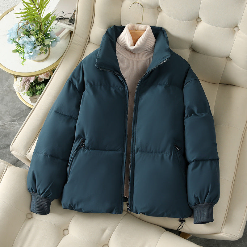 Giacca invernale imbottita blu scuro su poltrona beige, con collo alto e zip, perfetta per moda autunno-inverno. Stile casual e caldo.