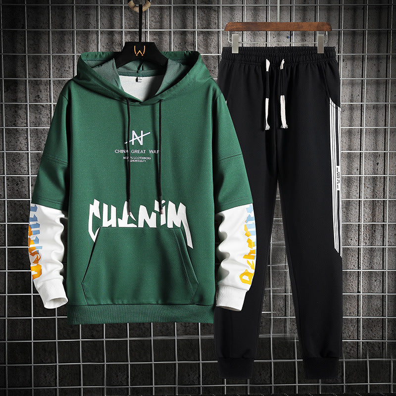 Felpa verde con cappuccio e scritte bianche, abbinata a pantaloni neri con strisce laterali bianche. Completo sportivo casual per uomo.
