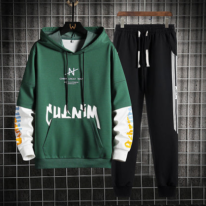 Felpa verde con cappuccio e scritte bianche, abbinata a pantaloni neri con strisce laterali bianche. Completo sportivo casual per uomo.