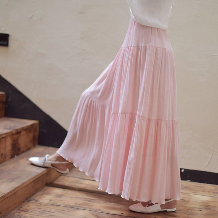 Gonna lunga rosa plissettata indossata da una donna su scale in legno, moda femminile elegante, abbinata a scarpe bianche.