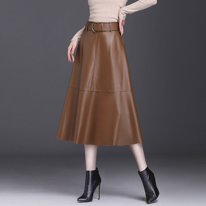 Gonna midi in pelle marrone con cintura, abbinata a stivaletti neri e maglione beige. Moda autunnale elegante e chic per donna.
