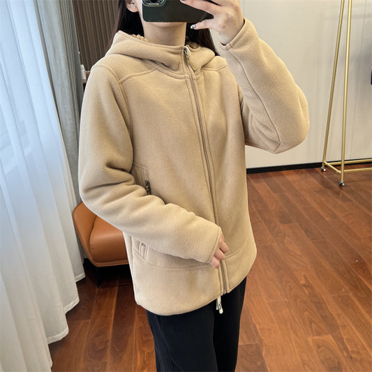 Donna con giacca beige in pile con cappuccio, chiusura a zip, in una stanza con pavimento in legno. Abbigliamento casual autunnale.