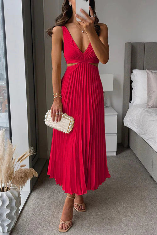 Donna in abito rosso plissettato con scollo a V, borsa bianca con perle, sandali beige, in una camera moderna con letto e finestra panoramica.