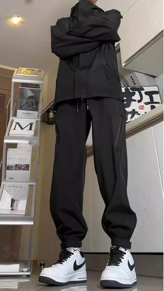 Uomo in tuta sportiva nera con scarpe Nike bianche e nere, in piedi in un interno moderno. Abbigliamento casual, moda streetwear.