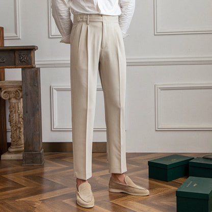 Pantaloni eleganti beige da uomo, taglio classico, abbinati a mocassini chiari. Stile formale, pavimento in legno, scatole verdi sullo sfondo.