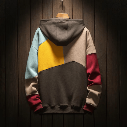 Felpa con cappuccio multicolore, design a blocchi, appesa su sfondo in legno. Moda casual, abbigliamento autunnale, stile urbano.