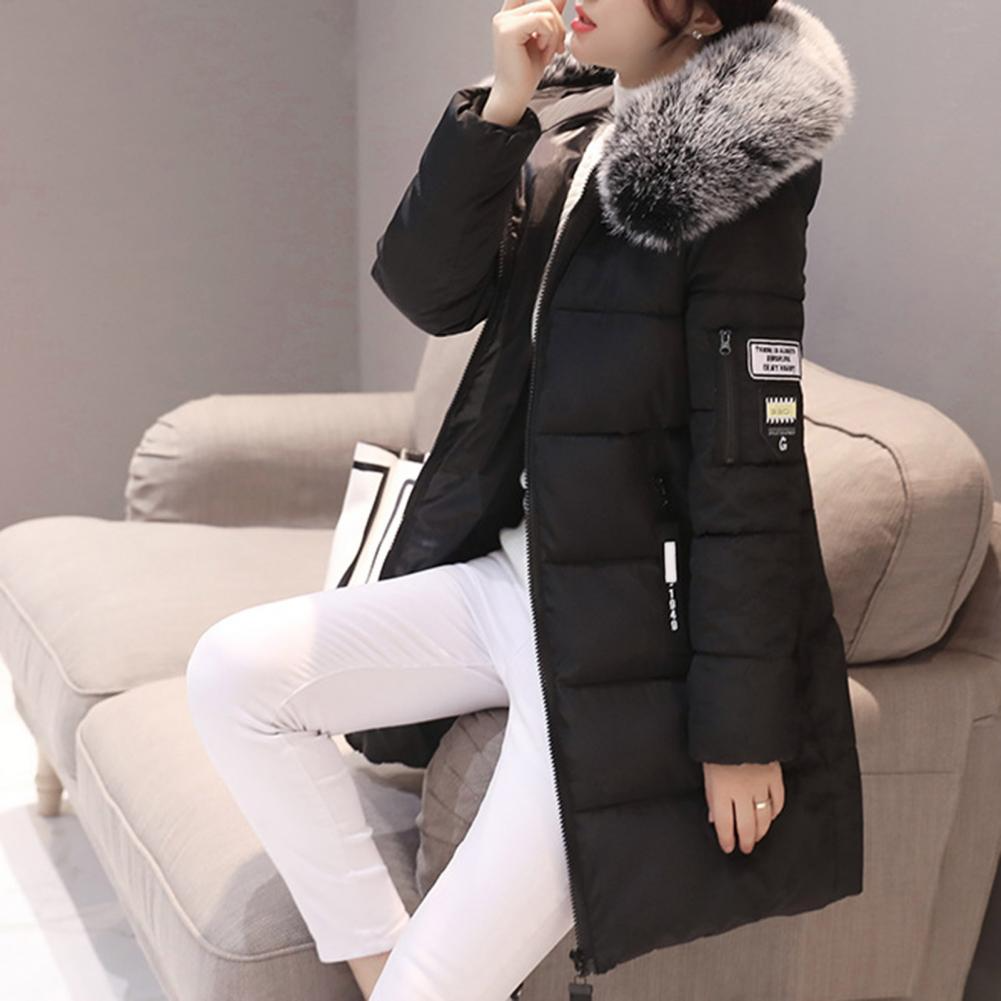 Giacca invernale nera con cappuccio in pelliccia sintetica, indossata da una persona seduta su un divano. Stile elegante e moderno.
