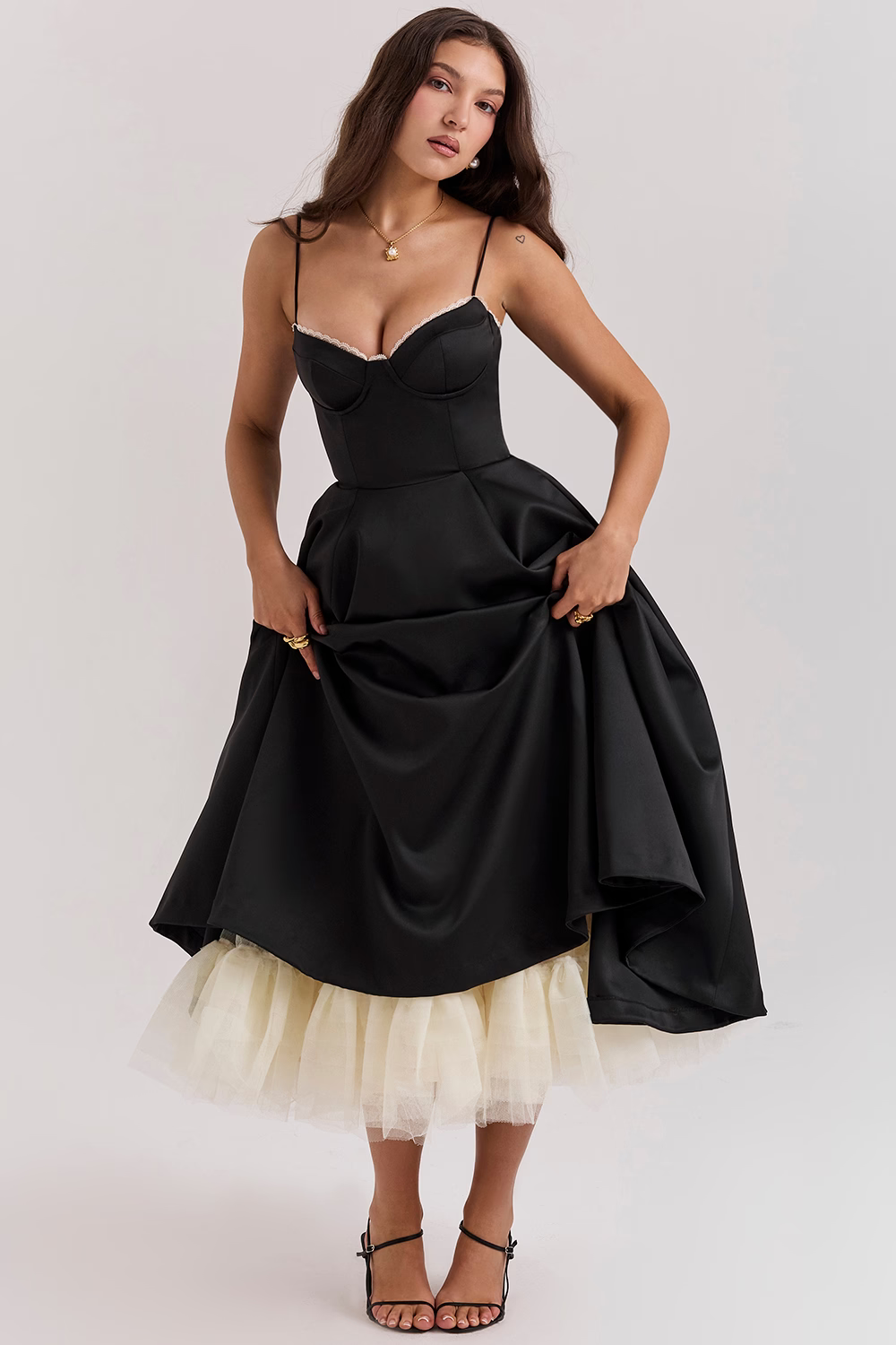Donna in abito nero elegante con spalline sottili e gonna ampia, dettagli in tulle bianco, posa su sfondo neutro. Moda femminile, abbigliamento da sera.