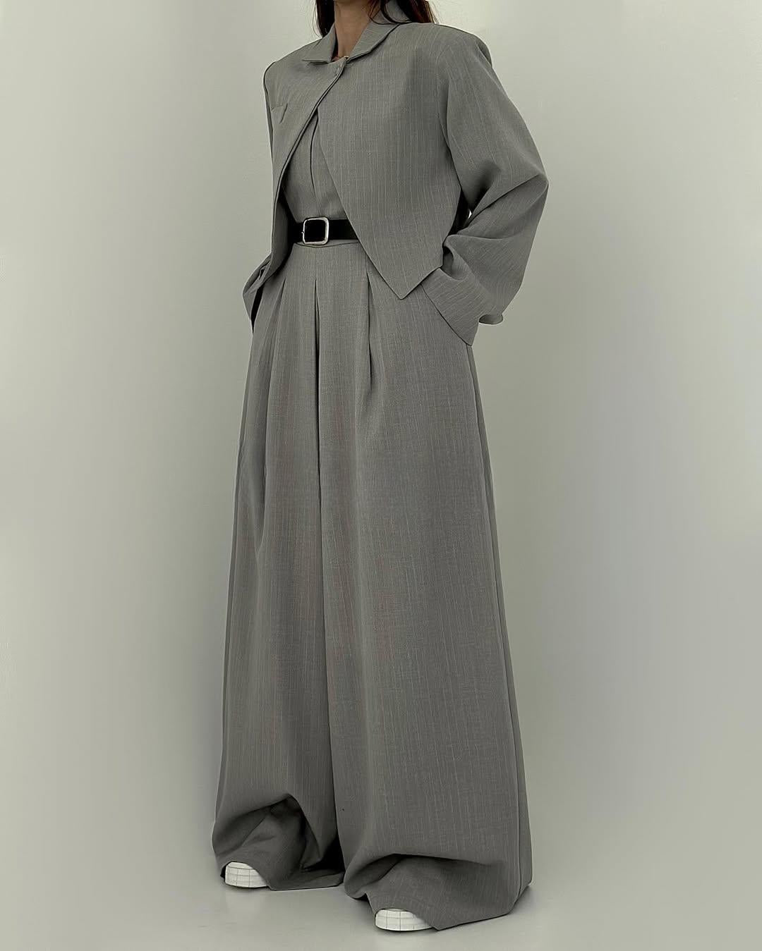 Donna in elegante completo grigio oversize, giacca e pantaloni larghi, cintura nera, scarpe bianche. Moda minimalista, abbigliamento formale.
