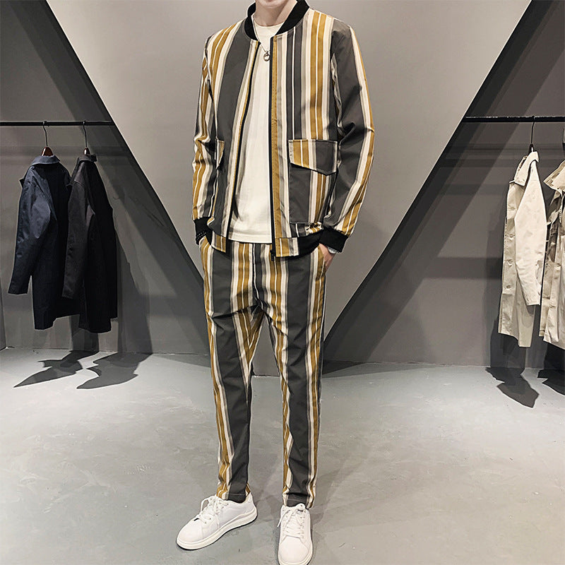 Completo uomo a righe verticali gialle, grigie e bianche, giacca e pantaloni coordinati, indossato con scarpe bianche, moda casual elegante.