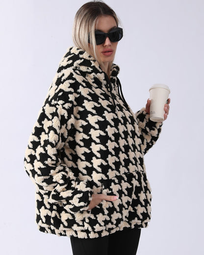Donna con occhiali da sole indossa felpa oversize in pile con motivo pied de poule bianco e nero, tiene bicchiere da caffè. Moda invernale casual.