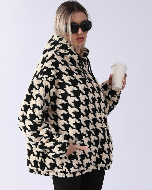 Donna con occhiali da sole indossa felpa oversize in pile con motivo pied de poule bianco e nero, tiene bicchiere da caffè. Moda invernale casual.