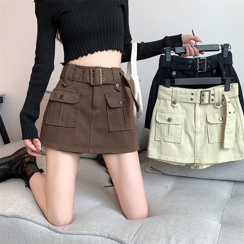 Donna con minigonna marrone a vita alta con cintura, tasche frontali. Tiene due minigonne simili, una nera e una beige. Moda autunnale casual.