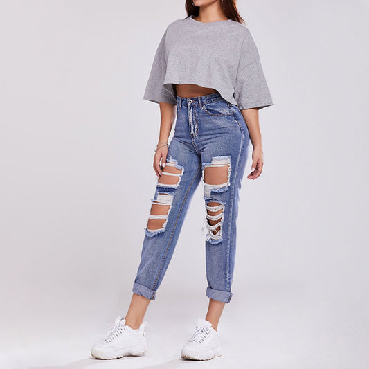 Donna in jeans strappati e maglietta grigia corta, scarpe da ginnastica bianche. Moda casual, abbigliamento trendy, stile urbano.