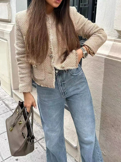 Donna con giacca in tweed beige, jeans a vita alta e borsa grigia di lusso. Moda autunnale elegante, look casual chic per strada.