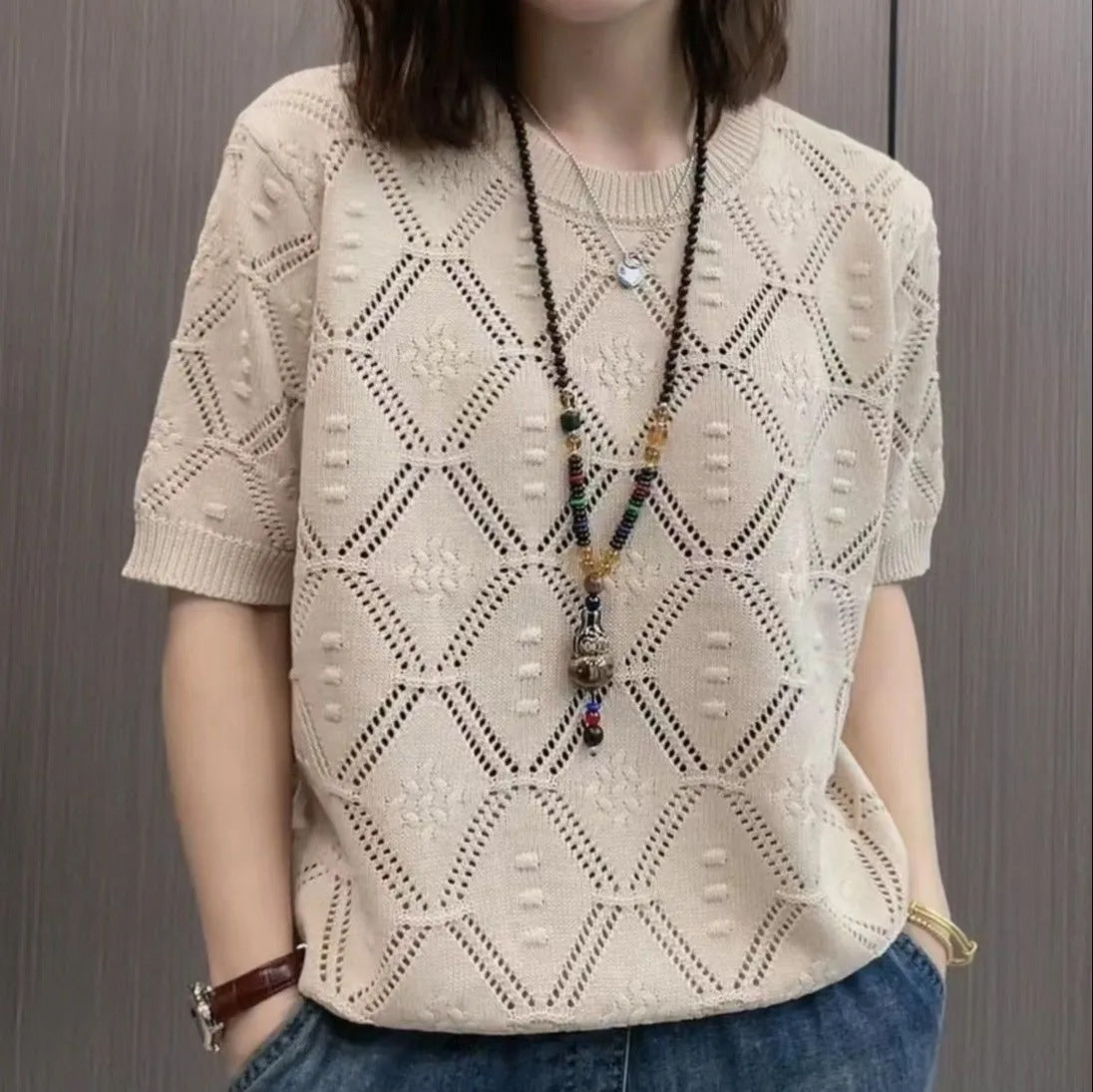 Maglia beige a maniche corte con motivo geometrico traforato, indossata con collana lunga e jeans. Moda casual donna, stile estivo elegante.