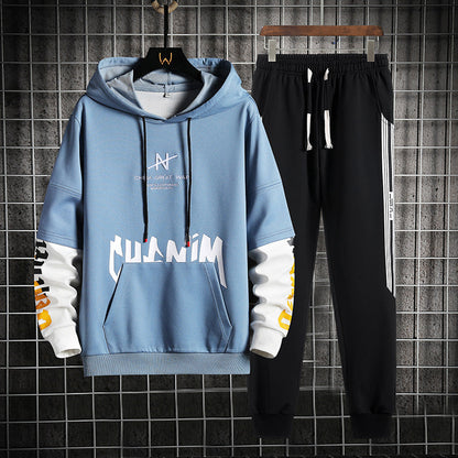Tuta sportiva uomo: felpa con cappuccio blu e pantaloni neri, design moderno, scritte bianche e gialle, ideale per abbigliamento casual e sportivo.
