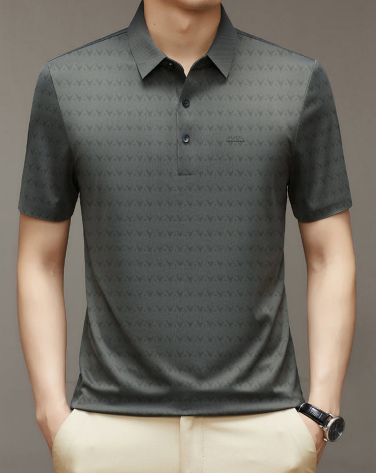 Uomo con polo grigia a maniche corte, motivo geometrico, colletto classico, abbinata a pantaloni beige. Stile casual elegante.