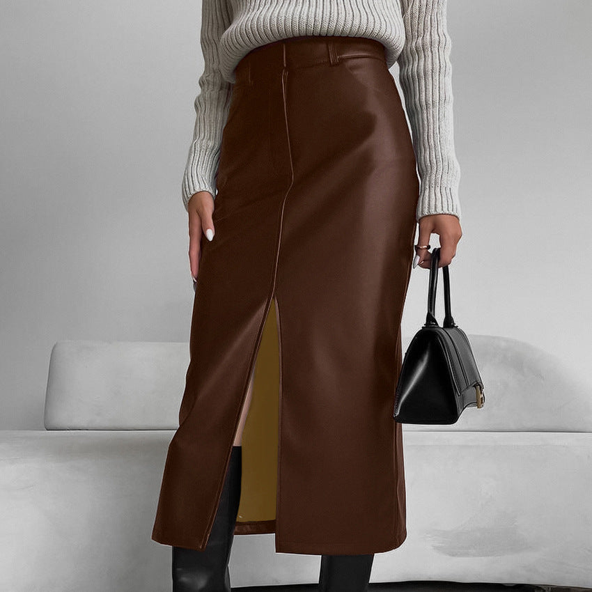Donna con gonna lunga in pelle marrone, maglione grigio e stivali neri, tiene una borsa nera. Moda autunnale elegante e sofisticata.