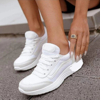 Scarpe da ginnastica bianche da donna, design moderno con suola spessa, indossate su pavimento grigio. Scarpe sportive eleganti e comode.