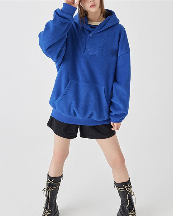 Donna con felpa blu oversize, pantaloncini neri e stivali alti. Moda casual autunnale, abbigliamento comodo e trendy. Sfondo bianco minimalista.