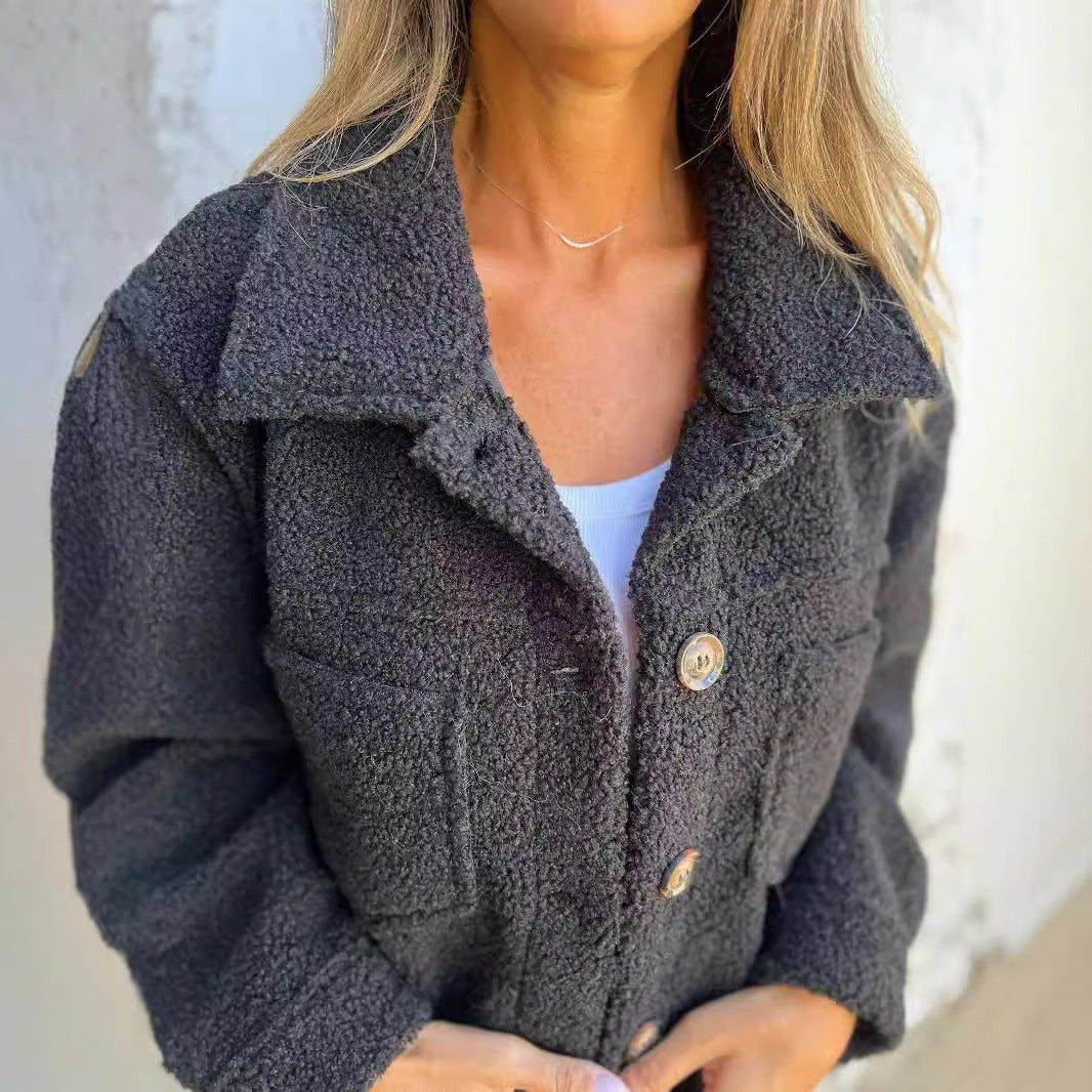 Donna con giacca in pile grigio scuro, bottoni in legno, indossa top bianco. Moda autunnale, abbigliamento casual, stile confortevole.