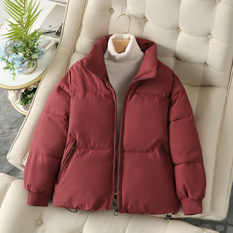Giacca invernale imbottita rossa su divano beige, con collo alto e zip, perfetta per moda autunno inverno. Stile casual e caldo.