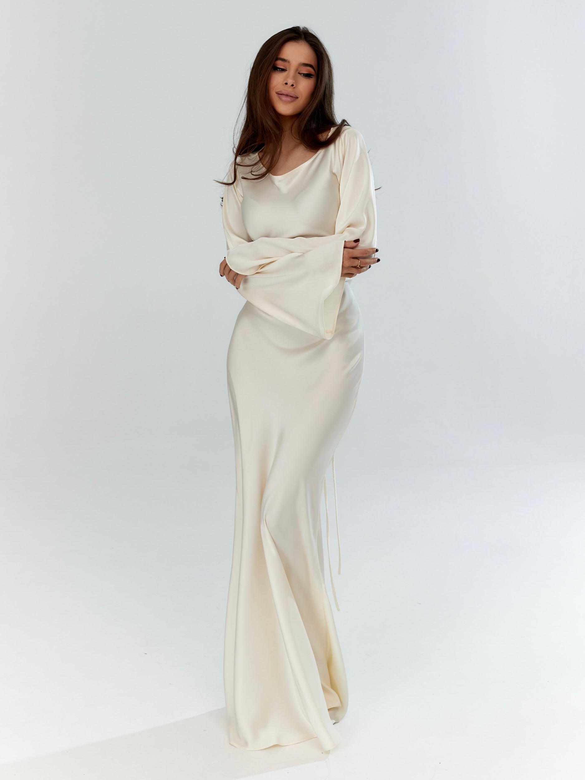 Donna in abito da sera bianco elegante, maniche lunghe, posa su sfondo bianco. Moda femminile, abbigliamento elegante, stile sofisticato.