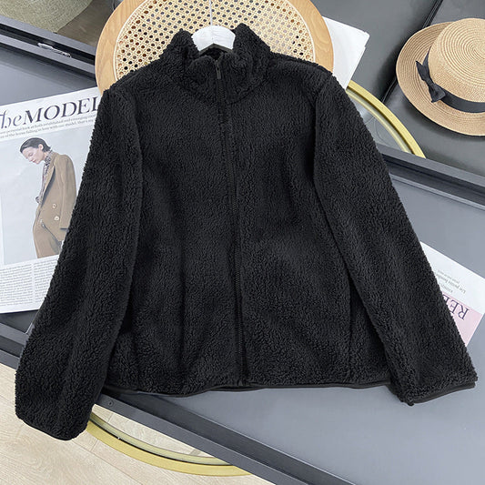Giacca in pile nero su tavolo, accanto a rivista di moda e cappello di paglia. Abbigliamento invernale caldo, stile casual.