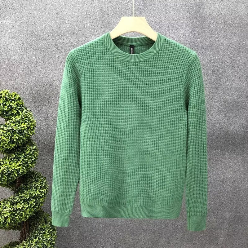 Maglione verde in maglia a trama grossa su appendiabiti, sfondo grigio. Moda uomo, abbigliamento invernale, stile casual elegante.