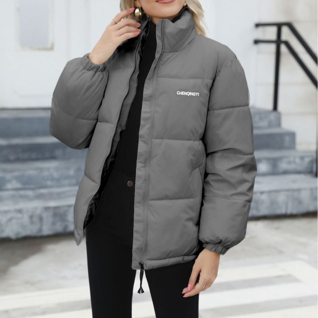 Donna con giacca invernale grigia imbottita, moda autunno-inverno, abbigliamento caldo e casual, scalinata urbana sullo sfondo.
