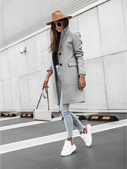 Donna alla moda con cappotto grigio, jeans strappati, sneakers bianche e cappello marrone, cammina su strada urbana. Borsa a tracolla elegante.