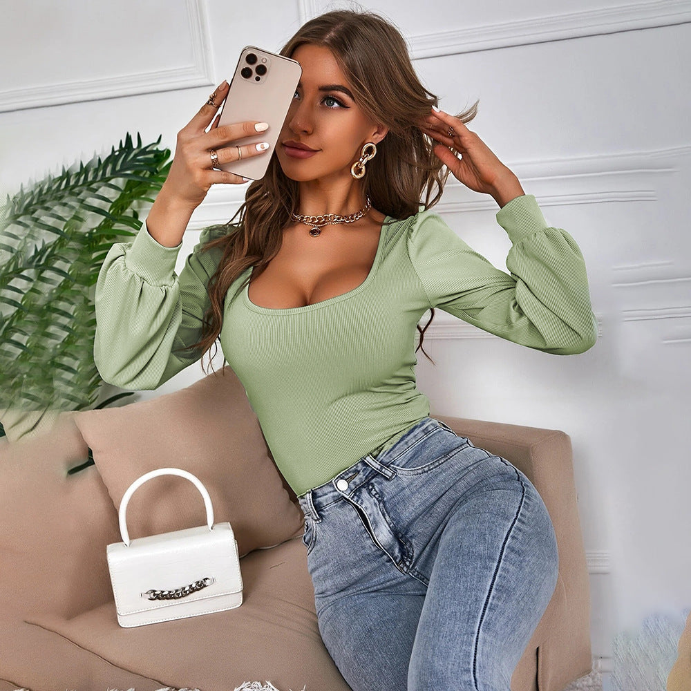 Donna con smartphone, indossa maglia verde e jeans, seduta su divano beige. Borsa bianca con catena in primo piano. Stile moda casual elegante.