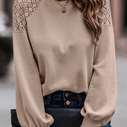Maglione beige a maniche lunghe con dettagli traforati sulle spalle, abbinato a jeans blu scuro. Stile casual elegante per moda autunnale.