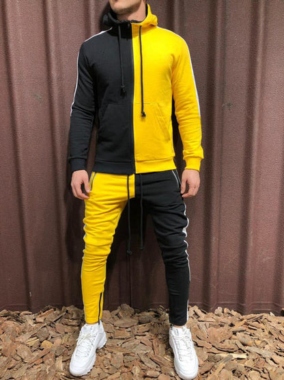Tuta sportiva bicolore giallo e nero, uomo in piedi su sfondo marrone, scarpe bianche. Abbigliamento casual, moda streetwear.